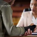 Mężczyzna z opaską na ręce rozmawia z prawniczką. Prawdopodobnie omawiają oświadczenie wypadkowe.