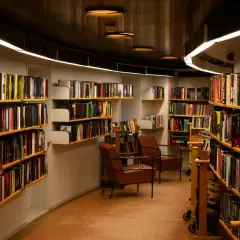 Wnętrze biblioteki z regałami pełnymi książek. Wygodne fotele zapraszają do lektury, a każdy tom czeka na swojego bibliotekarza.