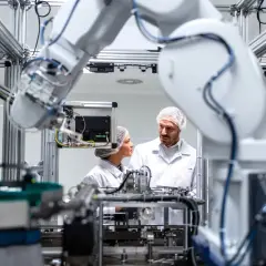 Mechatronik w białej szacie laboratoryjnej analizuje działanie robota przemysłowego.