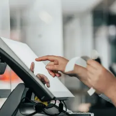 Sprzedawca obsługuje kasę dotykową, dotykając ekranu i trzymając paragon.