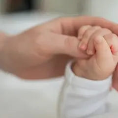 Dłoń dorosłego trzymająca dłoń niemowlaka.