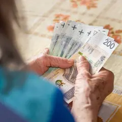 Dłonie starszej osoby liczą banknoty. W tle widać obrus. Tabela 13 emerytura 2026.