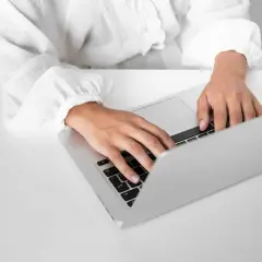 Dłonie piszące na klawiaturze laptopa na białym biurku.
