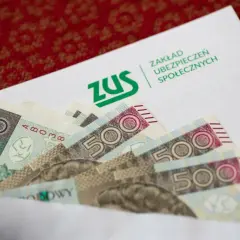 ZUS odszkodowania cennik tabela: banknoty 100 i 500 zł w kopercie z logo ZUS.