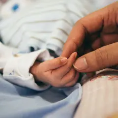 Dłoń rodzica obejmuje maleńką dłoń dziecka. To symbol miłości i troski, a także przygotowań do złożenia wniosku o urlop macierzyński.