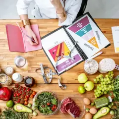 Intendentka planuje zdrowe posiłki, analizując piramidę żywienia i rozkład makroskładników. Na stole świeże produkty, suplementy i miarka.
