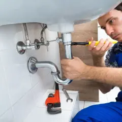Monter instalacji sanitarnych dokręca kluczem syfon pod umywalką.