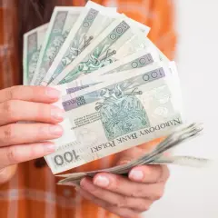 Ręce trzymające stos banknotów 100 zł. Zastanawiasz się, ile wynosi zasiłek dla bezrobotnych?