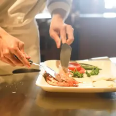 Kucharz przygotowuje danie z krewetek i warzyw, ćwicząc umiejętności do egzaminu zawodowego gastronomia.