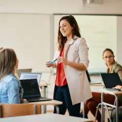 Nauczycielka wyjaśnia studentom, jak zostać nauczycielem zawodu. Uczniowie pracują na laptopach w sali lekcyjnej.