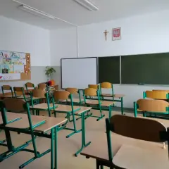Pusta klasa szkolna z rzędami ławek i krzeseł. Na ścianie tablica, projektor i dziecięce rysunki. Odwołane zajęcia w szkołach sprawiają, że sale wyglądają tak.