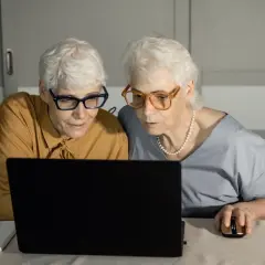 Dwie starsze kobiety w okularach patrzą na ekran laptopa.