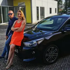 Instruktor nauki jazdy i kursantka pozują przy czarnym aucie z literą "L" na dachu.