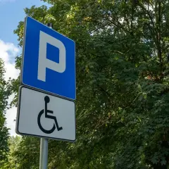 Niebieski znak "P" i biały znak z symbolem wózka inwalidzkiego. To miejsce parkingowe dla osób z niepełnosprawnościami, które posiadają odpowiednią kartę parkingową.