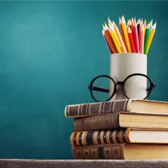 Stos książek, okulary i kredki na tle tablicy. To symbol wiedzy, która otwiera drzwi do kariery, nawet jeśli to co to znaczy wykształcenie średnie branżowe.