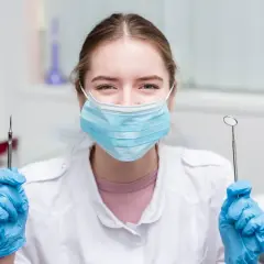 Uśmiechnięta asystentka stomatologiczna w maseczce i rękawiczkach trzyma narzędzia. Czas na egzamin!