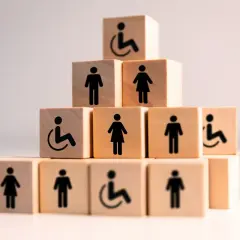 Drewniane klocki z symbolami osób i wózka inwalidzkiego ułożone w piramidę.