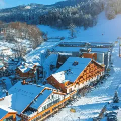 Idealne miejsce na ferie zimowe: ośnieżone góry, hotel z drewnianą elewacją i wyciąg krzesełkowy.