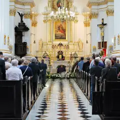 Uroczystość pogrzebowa w kościele. Ludzie stoją w ławkach, żegnając zmarłego teścia.