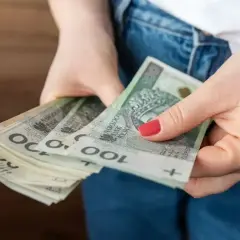 Dłonie trzymające stos polskich banknotów 100 zł.