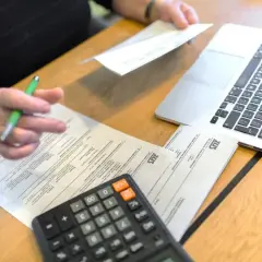 Osoba z długopisem analizuje dokumenty ZUS, kalkulator i laptop obok. Przygotowania do złożenia wniosku o emeryturę pomostową.