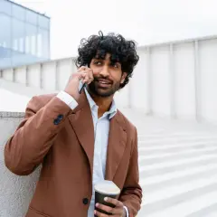 Mężczyzna w brązowej marynarce rozmawia przez telefon, trzymając kubek kawy.