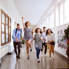 Uśmiechnięci uczniowie biegną korytarzem szkolnym. Wykształcenie średnie otwiera drzwi do radości i wspólnych chwil.