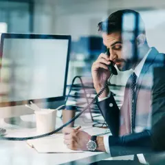 Biznesmen w garniturze rozmawia przez telefon, notując ważne informacje. Czasem czuje, że to **siła wyższa** kieruje jego karierą.