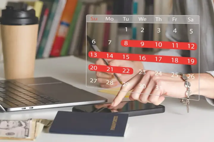 Planowanie urlopu: 26 dni wolnego do wykorzystania. Na biurku laptop, paszport, pieniądze i kalendarz.