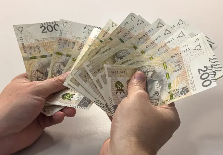 Ręce trzymające plik banknotów 200 zł. Dyskusja na forum: przeliczenie emerytury po 65 roku życia.
