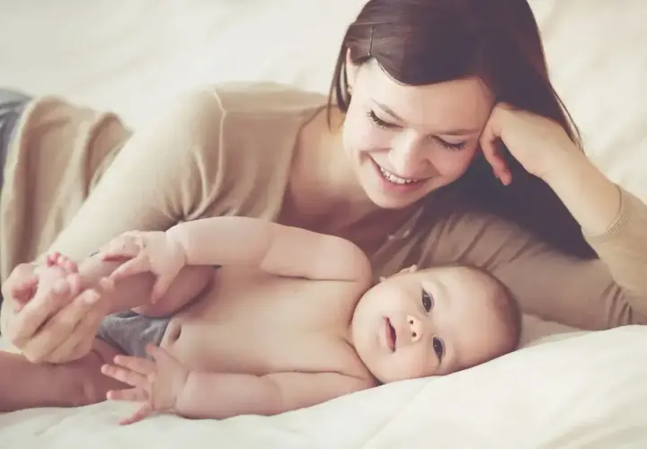 Uśmiechnięta mama na urlopie macierzyńskim bawi się nóżkami swojego dziecka.