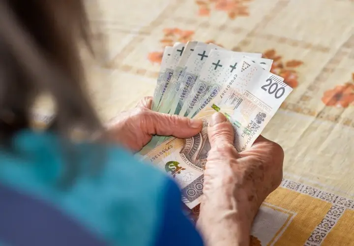 Dłonie starszej osoby liczą banknoty. W tle widać obrus. Tabela 13 emerytura 2026.