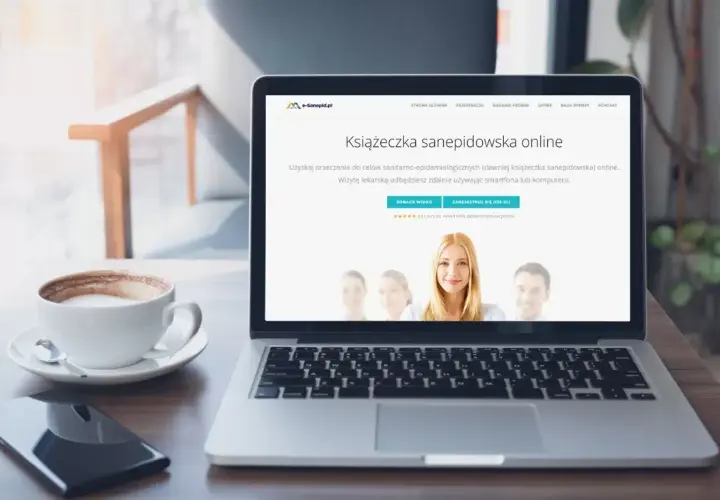 Laptop z kawą i telefonem. Na ekranie widnieje strona internetowa z ofertą "Książeczka sanepidowska online".