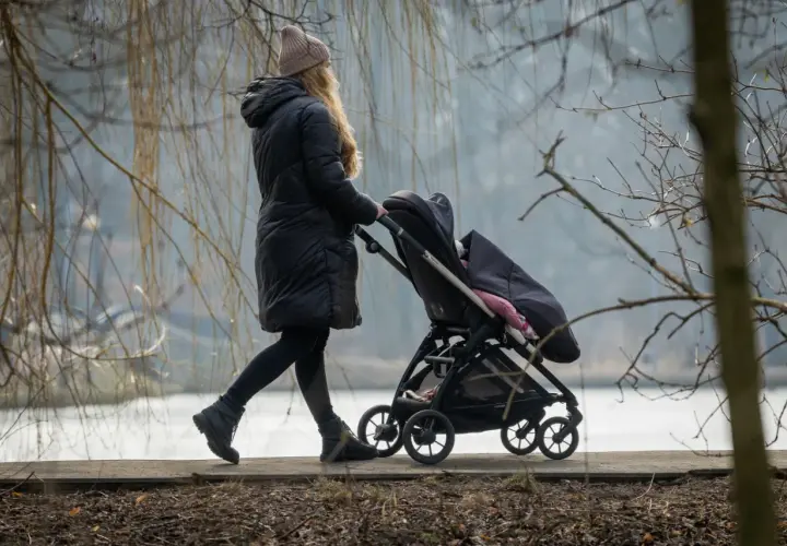 Kobieta na urlopie macierzyńskim spaceruje z dzieckiem w wózku. Zastanawia się, urlop macierzyński ile płatny, by zapewnić dziecku wszystko, co najlepsze.