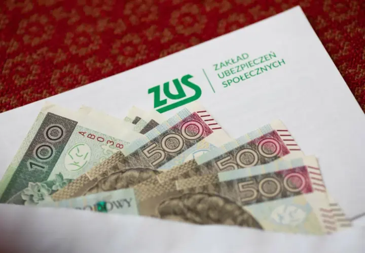 ZUS odszkodowania cennik tabela: banknoty 100 i 500 zł w kopercie z logo ZUS.