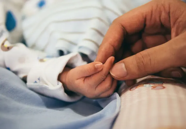 Dłoń rodzica obejmuje maleńką dłoń dziecka. To symbol miłości i troski, a także przygotowań do złożenia wniosku o urlop macierzyński.