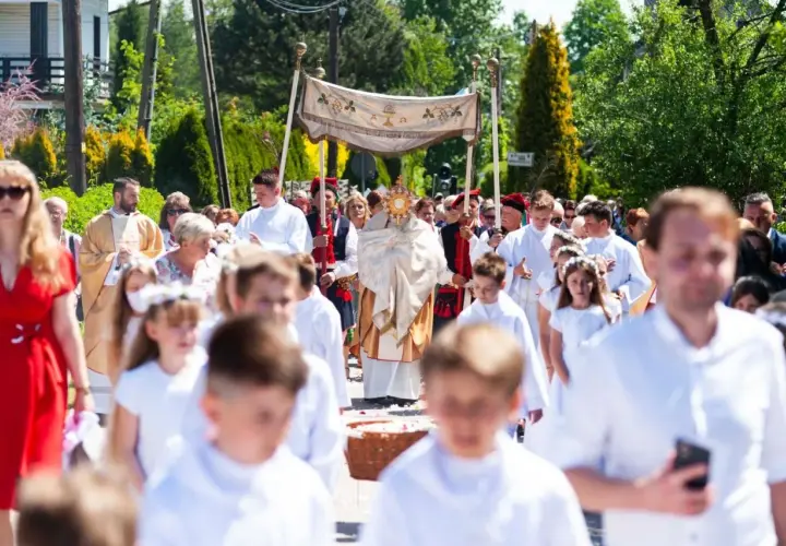 Procesja Bożego Ciała z monstrancją, księdzem i dziećmi w białych strojach.