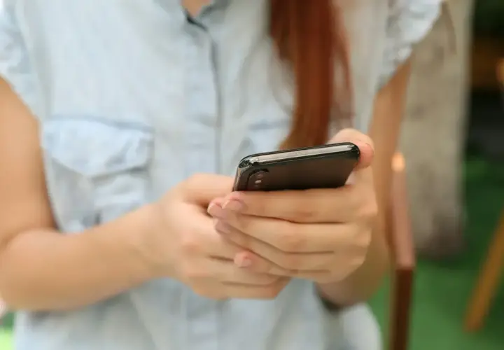 Kobieta w jasnej koszuli trzyma smartfon, szukając informacji, gdzie sprawdzić L4.
