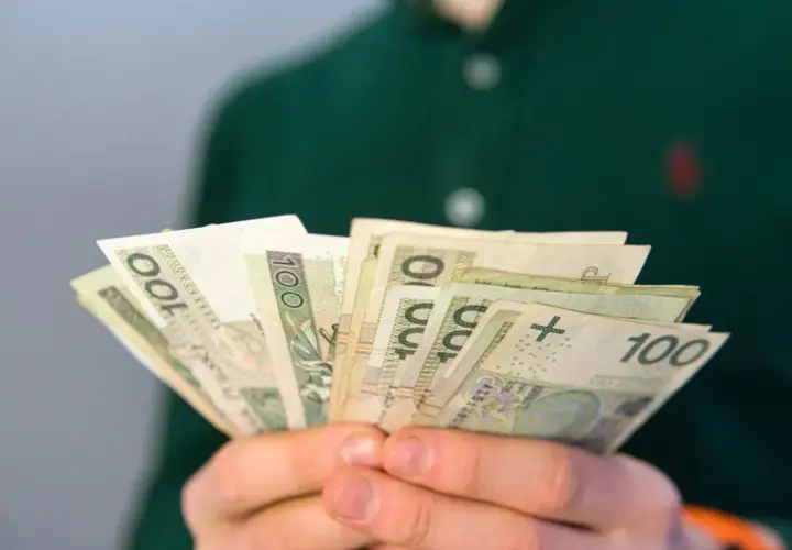 Dłonie trzymają wachlarz banknotów 100 zł. To może być pomocne przy pytaniu, co to jest renta rodzinna i jak ją uzyskać.
