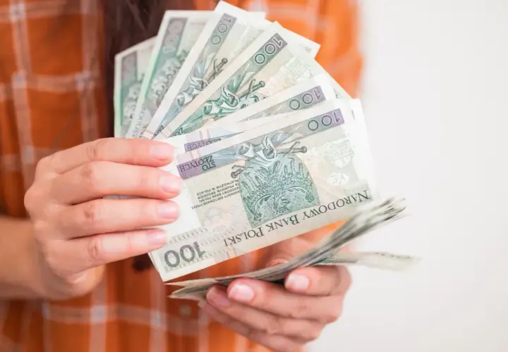Ręce trzymające stos banknotów 100 zł. Zastanawiasz się, ile wynosi zasiłek dla bezrobotnych?