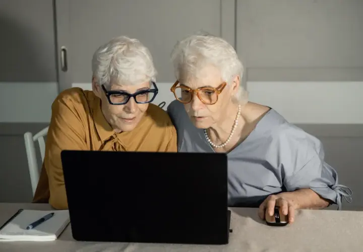 Dwie starsze kobiety w okularach patrzą na ekran laptopa.