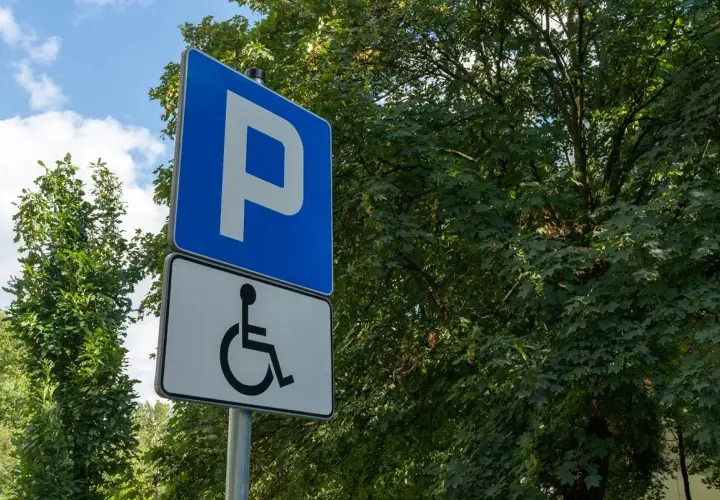 Niebieski znak "P" i biały znak z symbolem wózka inwalidzkiego. To miejsce parkingowe dla osób z niepełnosprawnościami, które posiadają odpowiednią kartę parkingową.