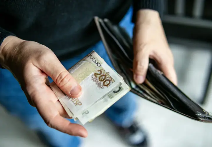 Ręce trzymają polskie banknoty 200 zł i pusty portfel. Zastanawiasz się, ile trwa zasiłek dla bezrobotnych?