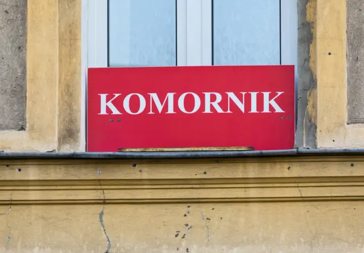 Czerwony szyld z napisem "KOMORNIK" nad oknem. Może oznaczać, że to miejsce, gdzie można dowiedzieć się o kwocie wolnej od zajęcia.