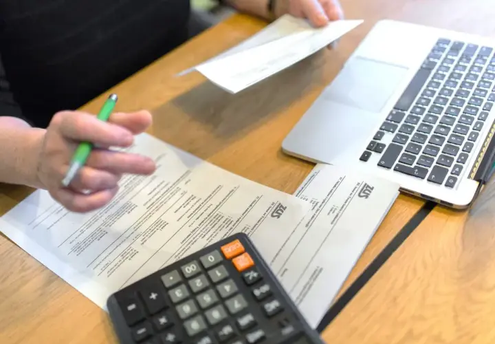 Osoba z długopisem analizuje dokumenty ZUS, kalkulator i laptop obok. Przygotowania do złożenia wniosku o emeryturę pomostową.