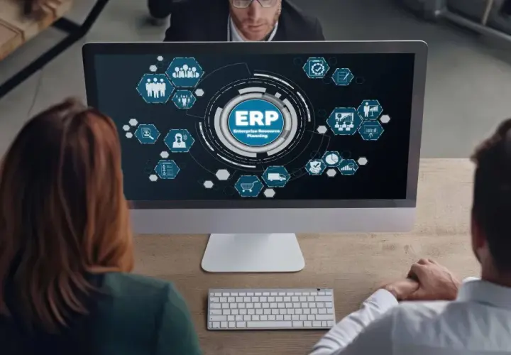 Zespół analizuje diagram ERP na ekranie komputera. Ikony symbolizują różne moduły systemu, od zarządzania zasobami ludzkimi po logistykę.
