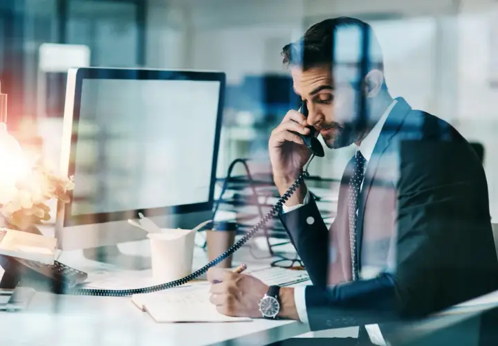 Biznesmen w garniturze rozmawia przez telefon, notując ważne informacje. Czasem czuje, że to **siła wyższa** kieruje jego karierą.