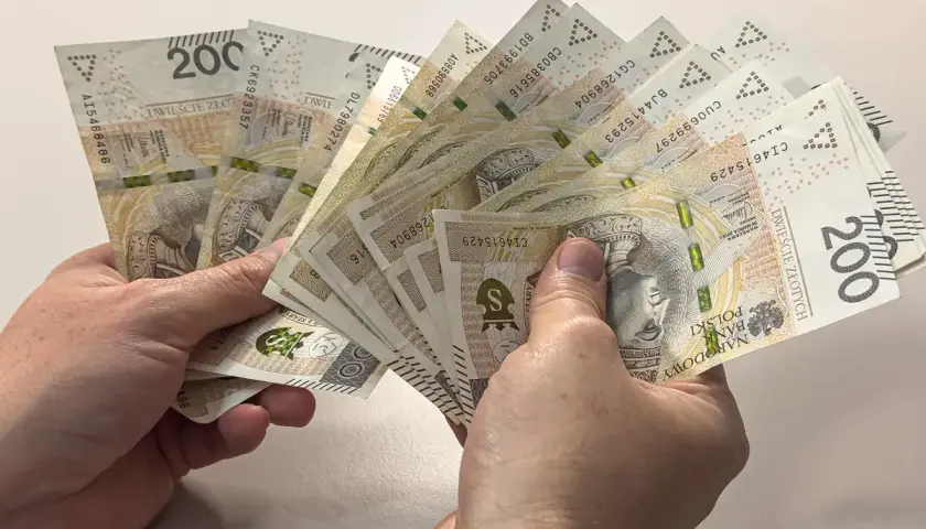 Ręce trzymające plik banknotów 200 zł. Dyskusja na forum: przeliczenie emerytury po 65 roku życia.