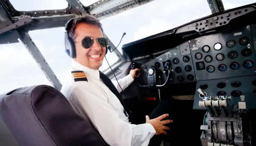 Uśmiechnięty pilot w okularach przeciwsłonecznych i słuchawkach w kokpicie samolotu. Zastanawiasz się, ile zarabia pilot samolotu?