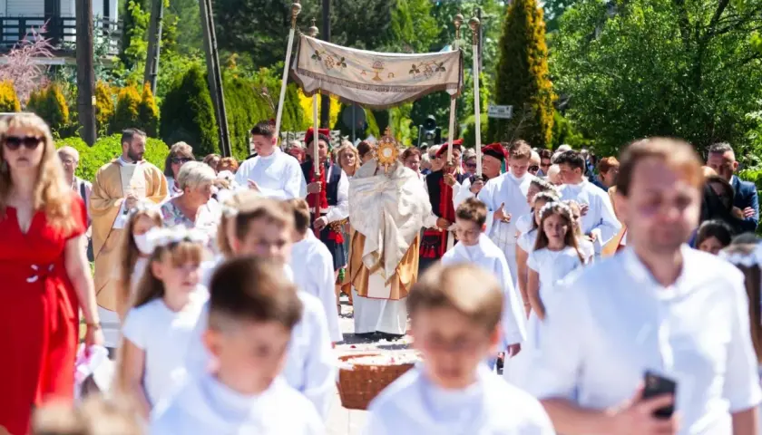 Procesja Bożego Ciała z monstrancją, księdzem i dziećmi w białych strojach.